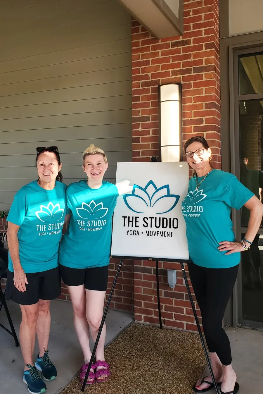 Studio teachers in teal shirts next to The Studio sign